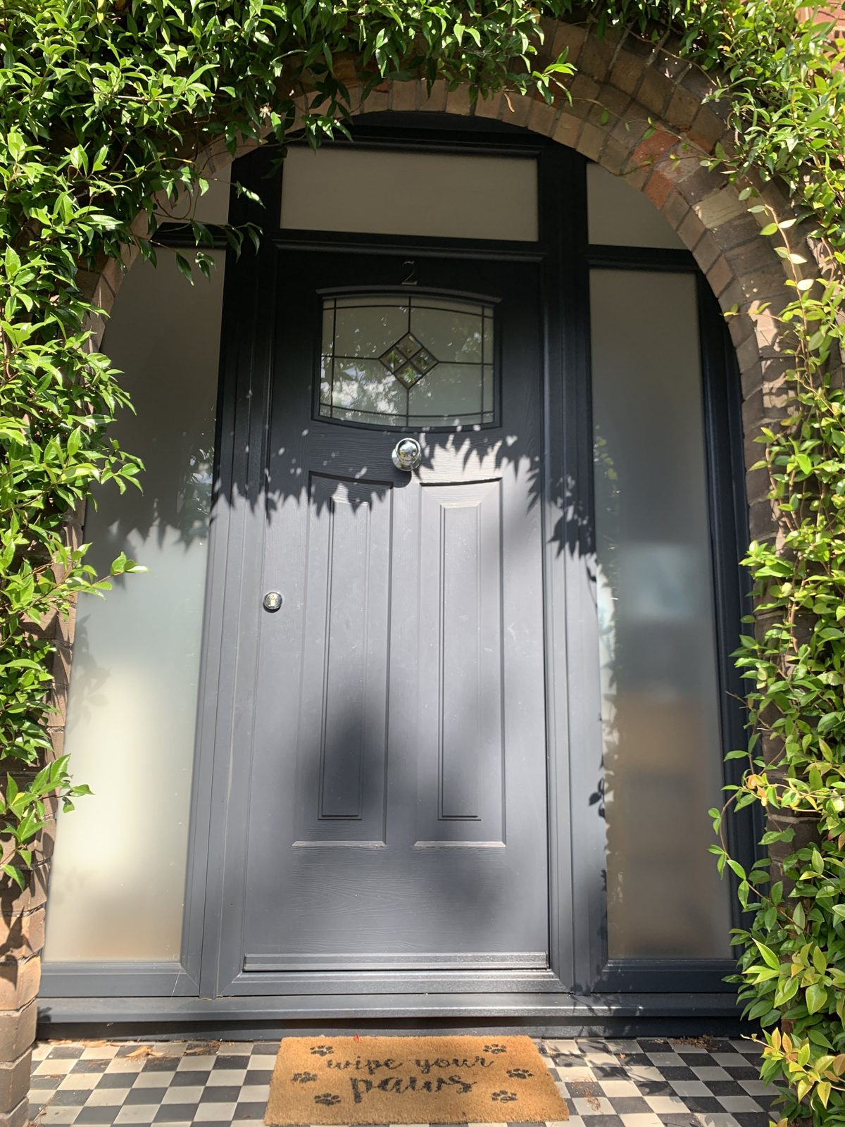 Black traditional Rockdoor with leaded feature glass, obscure sidelights and toplight in an arched opening, supplied by WGS Glazing